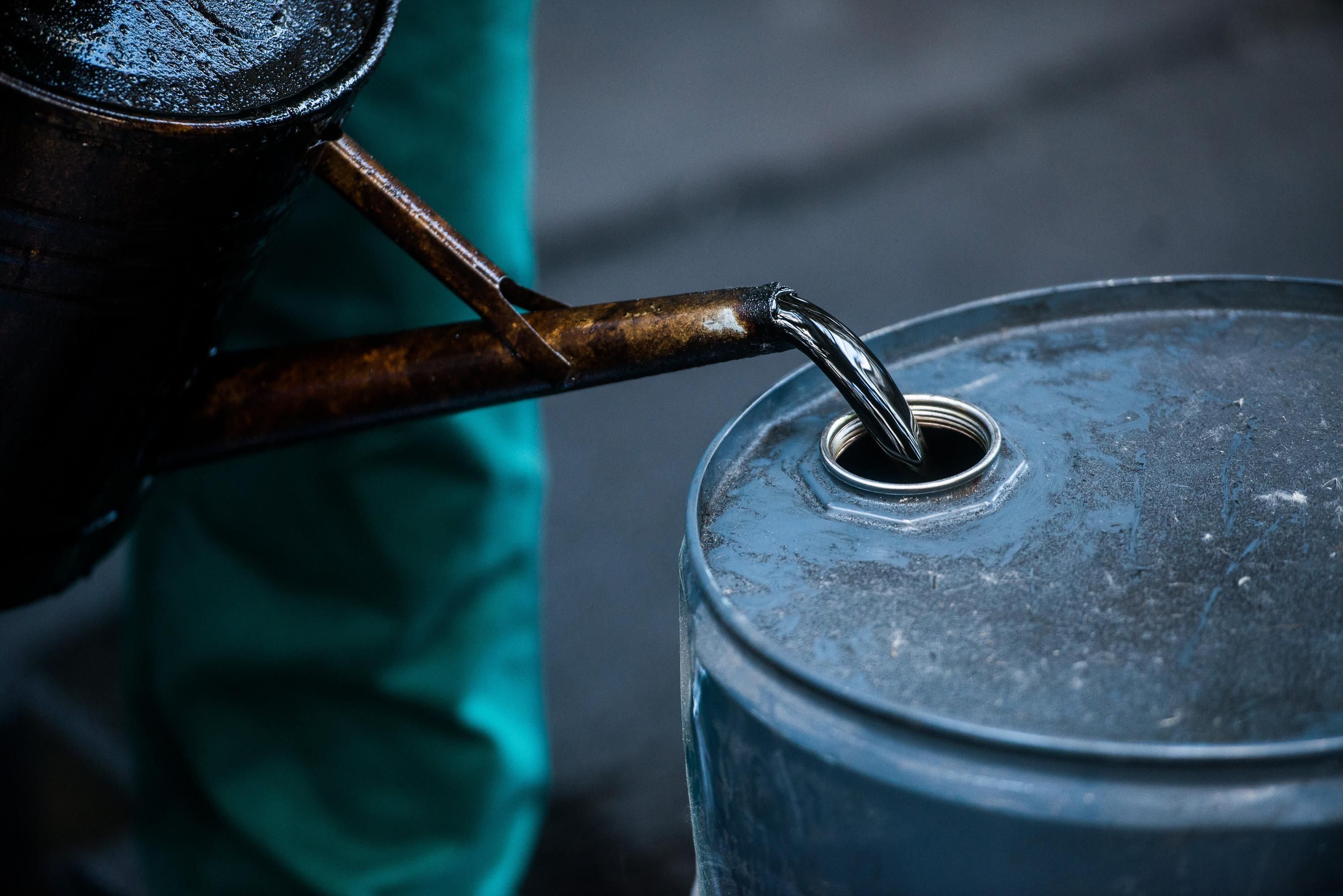 Рабочий наливает нефть в бочку